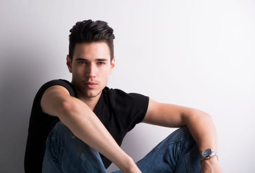 Handsome young man sitting on light background, looking at camera