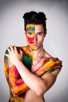Attractive young man shirtless, skin painted all over with bright Holi colors on light background