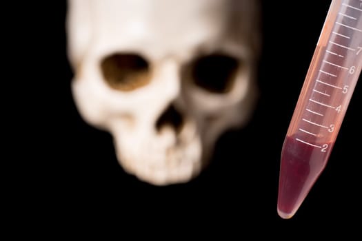 blood sample or other red liquid in testtube and blurry skull isolated on black background