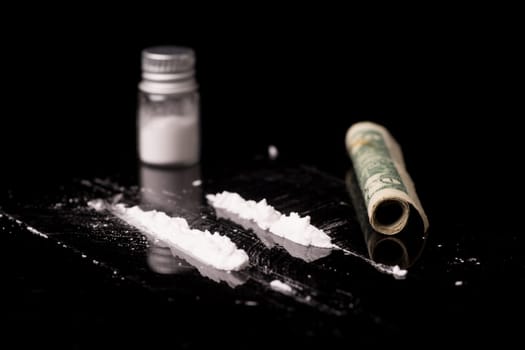 cocaine or other illegal drugs that are sniffed by means of a tube, isolated on black glossy background