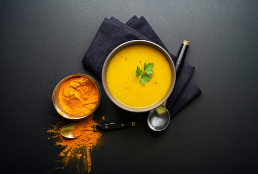 Healthy turmeric or curcuma cream soup on black background