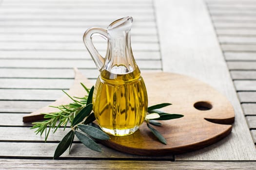 Olive oil with herbs and branch on wooden background