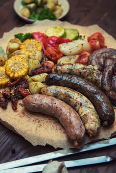 Grilled different meat and fish sausages with vegetables and spices on wooden background