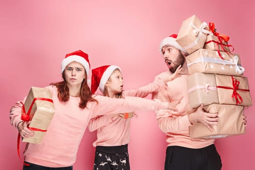 Father and mother give gifts to little daughter at pink studio background