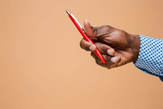 Male hand holding pencil, isolated on studio brown background