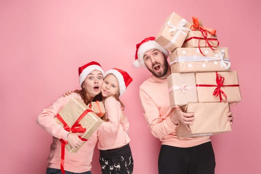 Father and mother give gifts to little daughter at pink studio background