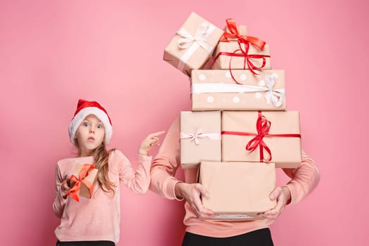 Portrait of a surprised little girl with her father holding a Christmas present at pink studio background