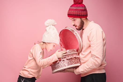 Portrait of a surprised little girl with her father holding a Christmas present at pink studio background