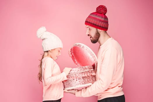 Portrait of a surprised little girl with her father holding a Christmas present at pink studio background