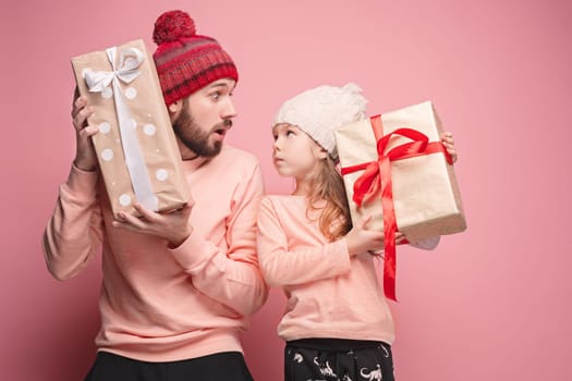 Portrait of a surprised little girl with her father holding a Christmas present at pink studio background
