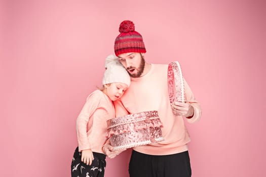 Portrait of a surprised little girl with her father holding a Christmas present at pink studio background