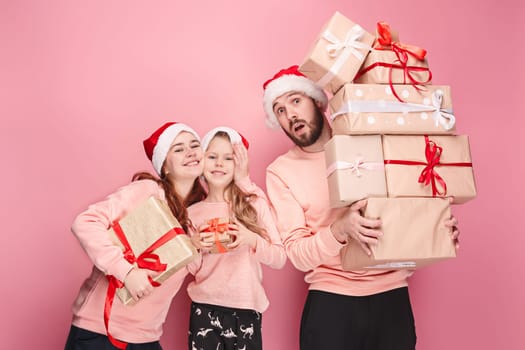 Father and mother give gifts to little daughter at pink studio background