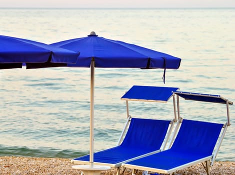 two sunbeds on a stony beach with calm sea in background