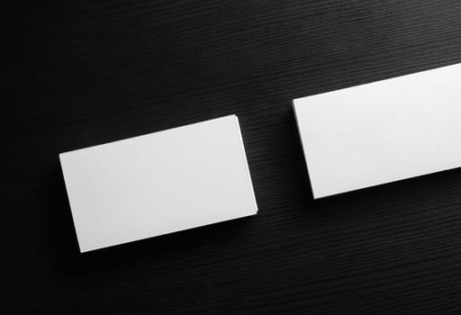 Blank white business cards on black wooden table background. Template for ID with plenty of copy space. Top view.
