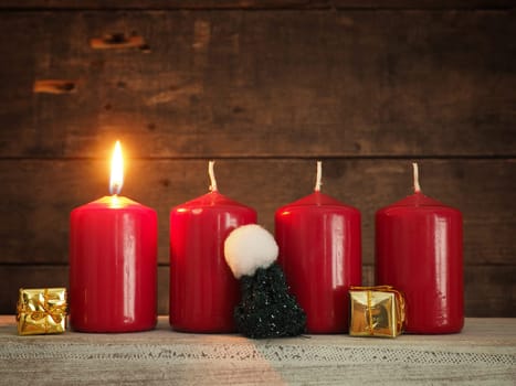 Four red Advent candles on a rustic wooden background, First candle is burning, Christmas concept background
