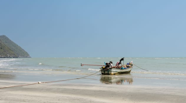 Small woodenl fishing boat (Longtail boat) anchored on beach at low tide in Thailand