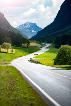 Road in mountains of Norway, Europe. Auto travel through scandinavia. Blue cloudy sky in background. White house in foreground.