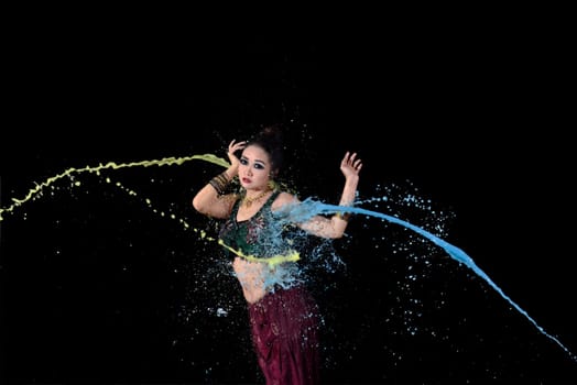 Exotic asian belly dancer dancing with colorful paint against black background