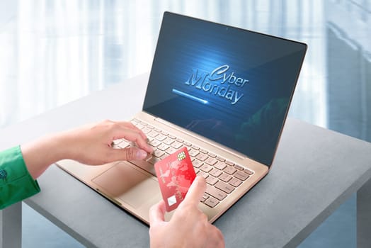 Hand holding credit card and using laptop with Cyber Monday sign on the screen on the desk. Cyber Monday concept