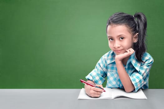 Smiling asian little girl doing her homework against chalkboard background