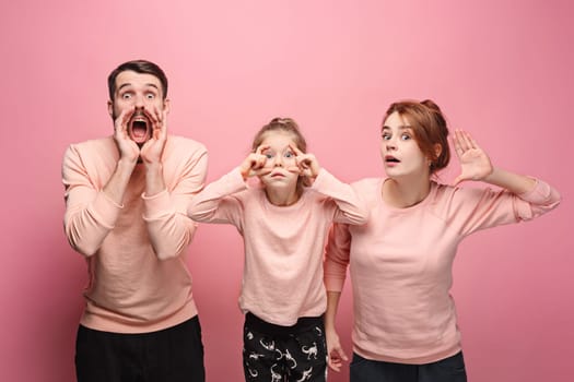 Surprised young family looking at camera on pink studio background