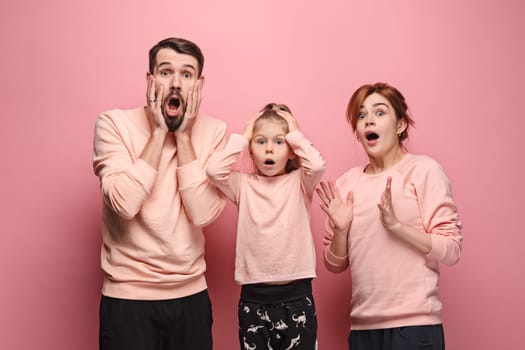 Surprised young family looking at camera on pink studio background