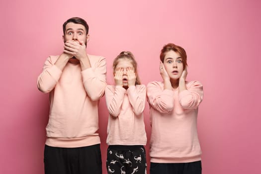 Surprised young family looking at camera on pink studio background. The concept of fear