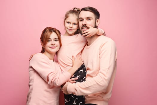 Happy young family with one little daughter posing together on pink studio background