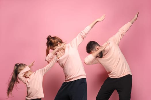 The dancing young family on pink studio background