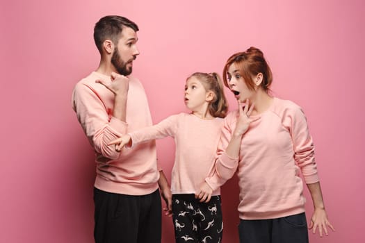 Surprised young family pointing left by fingers on pink studio background