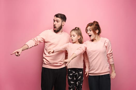 Surprised young family pointing left by fingers on pink studio background