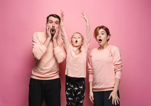 Surprised young family looking at camera on pink studio background