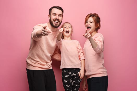 Surprised young family pointing up by fingers on pink studio background