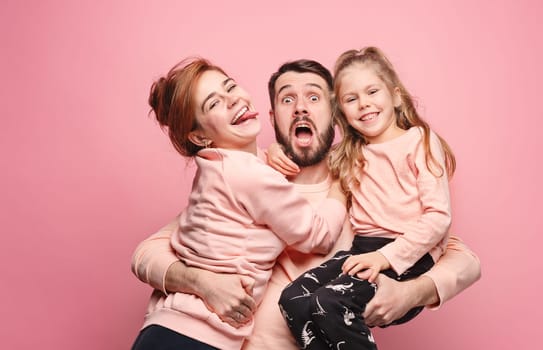 Happy young family with one little daughter posing together on pink studio background