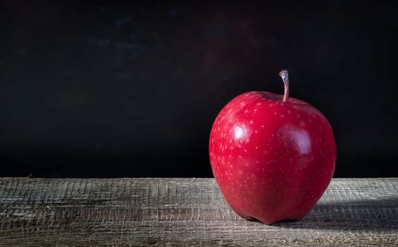 Single apple on a wooden table. Blurred dark background.