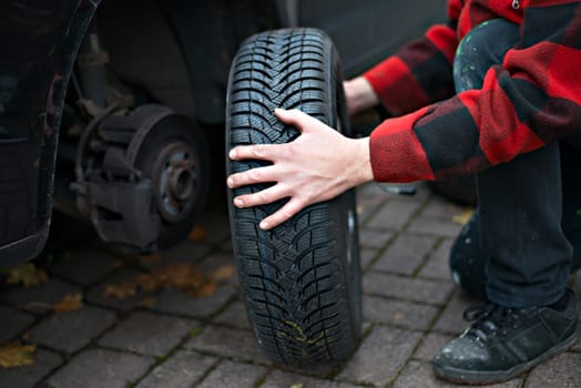 man in chequered jacket changing tyre on his car