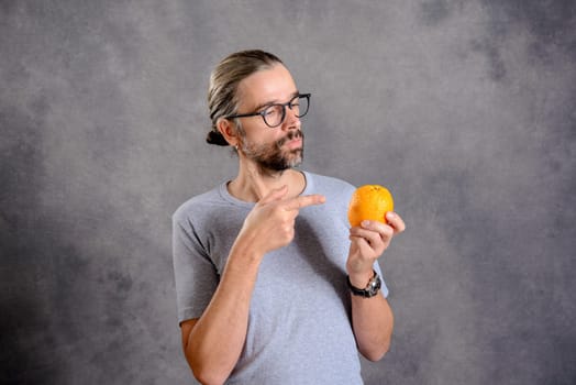 long haired young man with orange in front of gray background