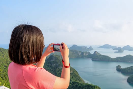 Woman tourist on peak viewpoint of Ko Wua Ta Lap island use camera take photos at beautiful nature landscape during sunrise over the sea in Mu Ko Ang Thong National Marine Park, Surat Thani, Thailand