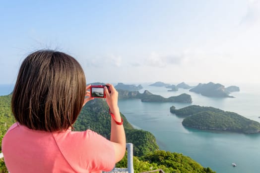 Woman tourist on peak viewpoint of Ko Wua Ta Lap island use camera take photos at beautiful nature landscape during sunrise over the sea in Mu Ko Ang Thong National Marine Park, Surat Thani, Thailand