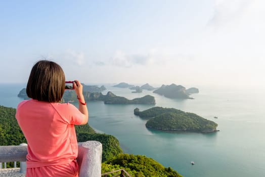 Woman tourist on peak viewpoint of Ko Wua Ta Lap island use camera take photos at beautiful nature landscape during sunrise over the sea in Mu Ko Ang Thong National Marine Park, Surat Thani, Thailand