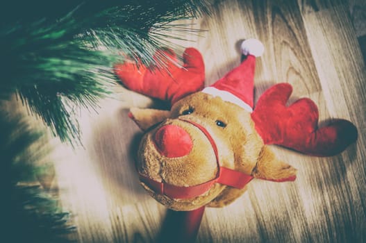 Stick plush reindeer toy over wooden floor close to Christmas Tree at home