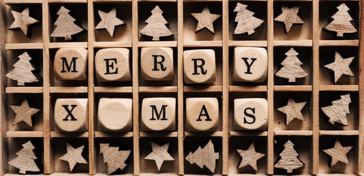 Small wooden dices in a box with the words Merry x-mas, star and tree shape decoration around