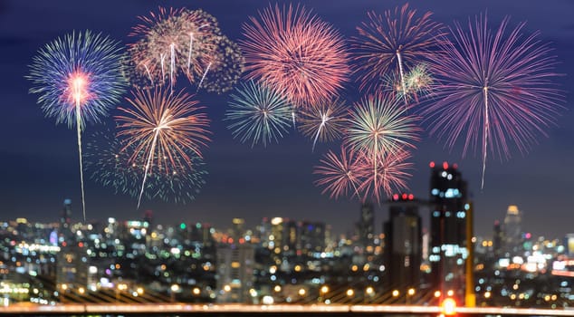 Colorful fireworks on blurred skyscrapers with city bokeh lights illuminated at night. Abstract New Year holiday or party background