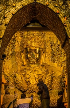 Devotees applying gold leaf to Mahamuni Buddha in Mandalay, Myanmar