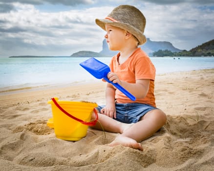Cute boy on the tropical beach playing toys