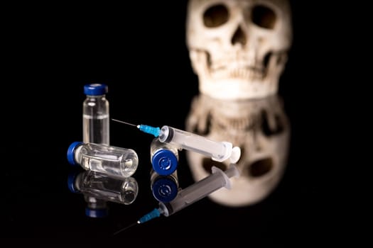 Skull, syringe and medical vials isolated on black blue background with glossy reflection