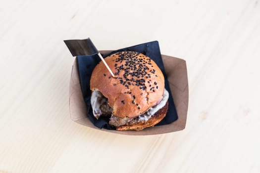 Hamburger on light brown wooden table, one bite taken out of it.