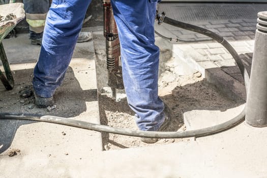 Builder worker with pneumatic hammer drill equipment breaking sidewalk asphalt on street