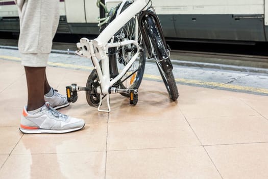 Young black guy waiting a commuter train with his small fold bicycle