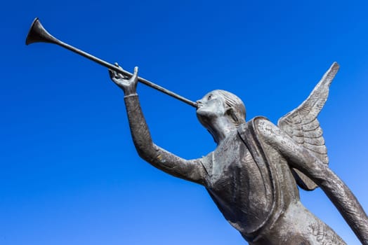 Statue of an angel playing a trumpet over blue sky